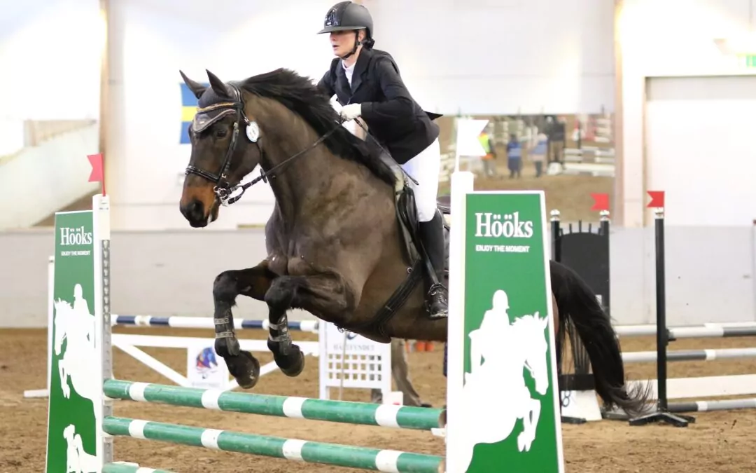 Ryttare hoppar hinder med häst inomhus