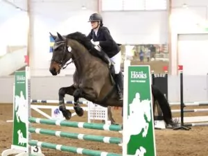 Ryttare hoppar hinder med häst inomhus